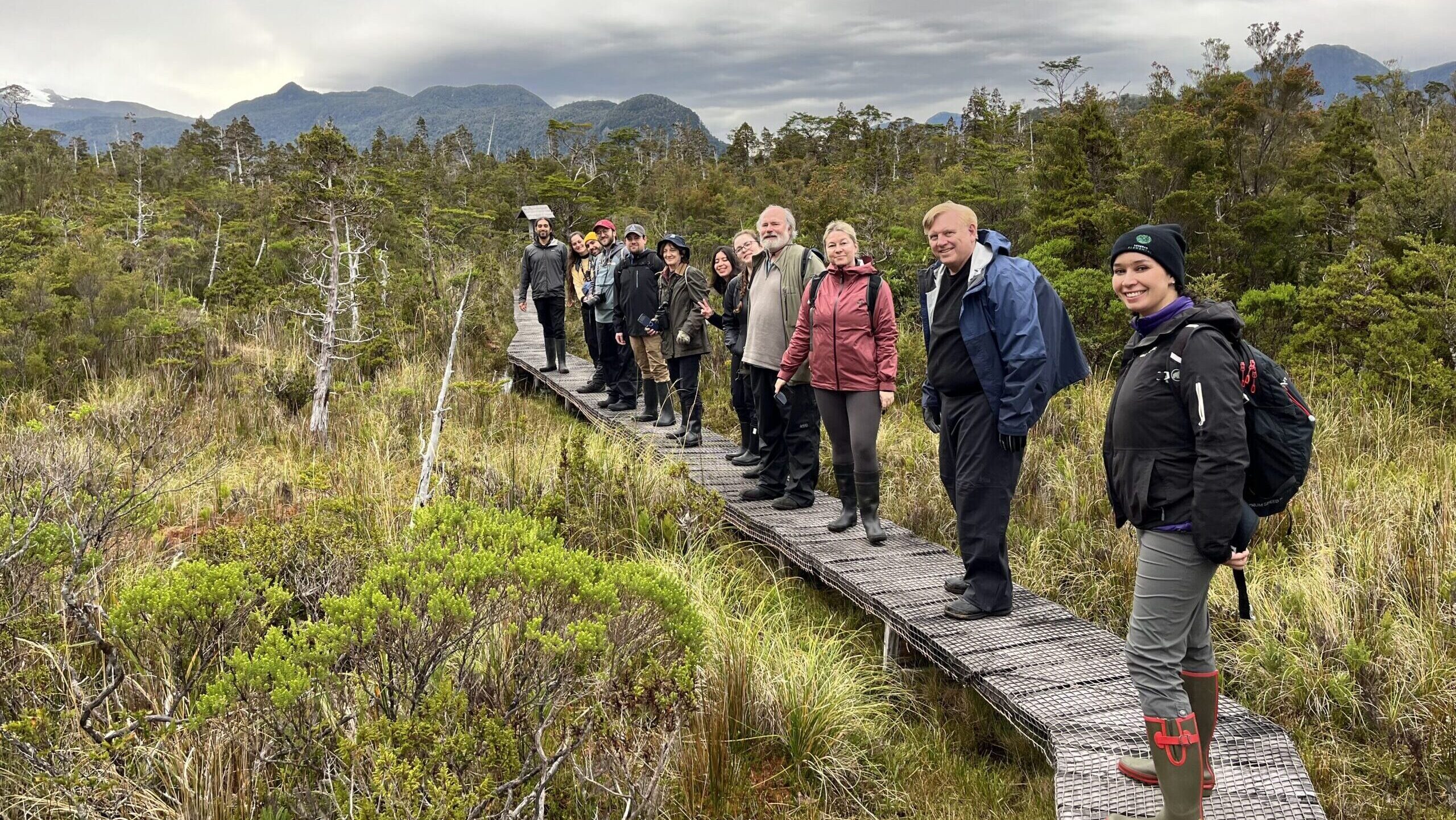 IMG_3738 Standing on a wooden path in a meadow, a group of nature guardians look over their shoulders and smile.