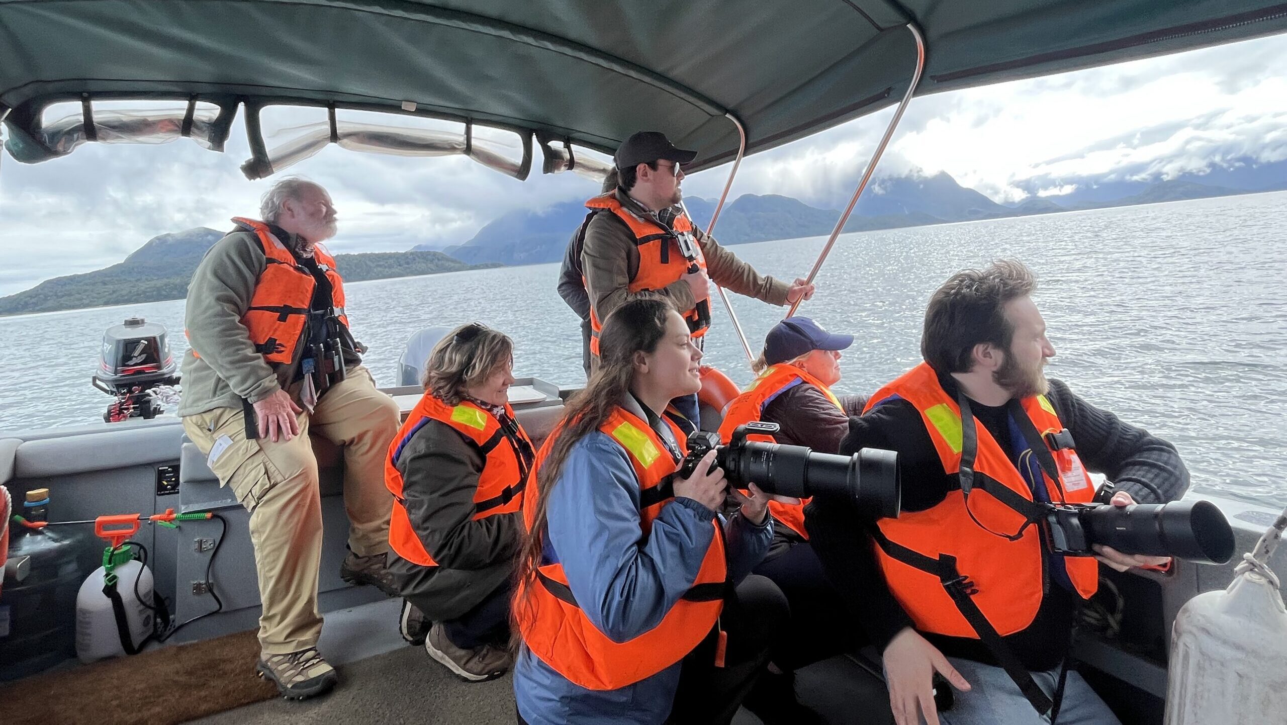 Six nature guardians wearing life jackets aboard a boat look out into the horizon in search of wildlife.